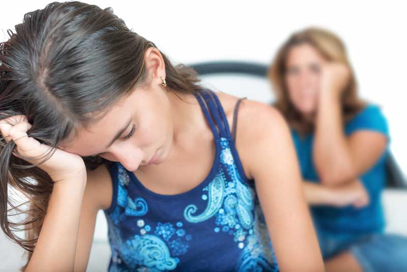A teen girl looks depressed or sad and her mother looks concerned.